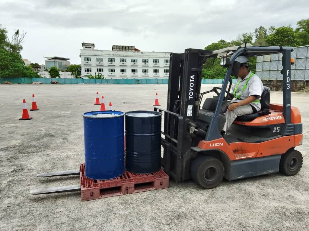 Operator forklift dengan PPE lengkap mengendalikan forklift di gudang secara selamat