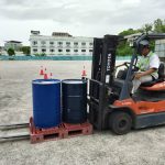 Operator forklift dengan PPE lengkap mengendalikan forklift di gudang secara selamat